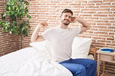 Young caucasian man waking up stretching arms at bedroom