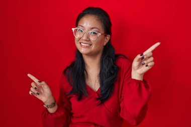 Asyalı genç bir kadın kırmızı arka planda duruyor. Kendine güvenen, parmaklarıyla farklı yönleri gösteren biri. reklam için kopyalama alanı 