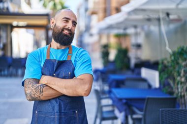 Young bald man waiter smiling confident standing with arms crossed gesture at coffee shop terrace