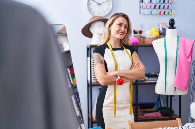 Young beautiful hispanic woman tailor smiling confident standing with arms crossed gesture at clothing factory