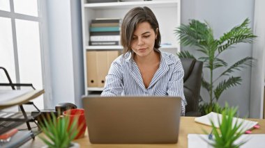 Genç, güzel İspanyol kadın çalışan, kendine güvenen, dizüstü bilgisayarına odaklanan, iş ofisinde sıkı çalışan, profesyonel başarısını gösteren.