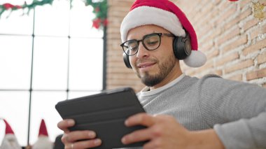 Touchpad kullanan İspanyol adam evde Noel süslemesi yaparak müzik dinliyor.