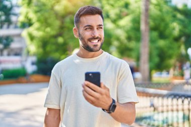 Parkta akıllı telefon kullanarak gülümseyen İspanyol genç adam.