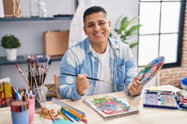 Young latin man artist smiling confident drawing on notebook at art studio