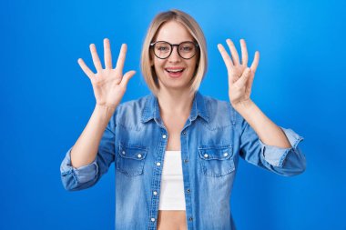 Young caucasian woman standing over blue background showing and pointing up with fingers number nine while smiling confident and happy. 