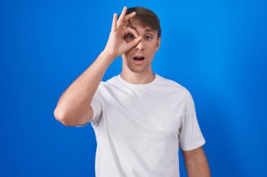 Beyaz, sarışın bir adam mavi arka planda dikiliyor. Şaşırmış yüz ifadesiyle şaşırmış bir şekilde hareket ediyor. Gözleri parmaklarından bakıyor. İnançsız ifade. 