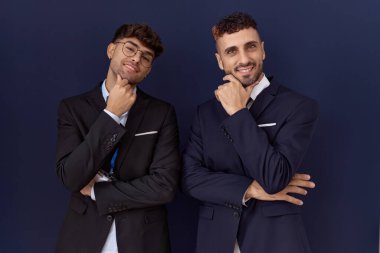 İki İspanyol iş adamı iş kıyafetleri içinde kameraya bakıp kollarını kavuşturup gülümseyerek çenelerini kaldırıyorlar. Olumlu düşünmek. 