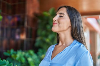 Young beautiful hispanic woman breathing with closed eyes at street