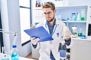 Laboratuvarda test tüpü tutan genç bilim adamı raporunu okuyor.