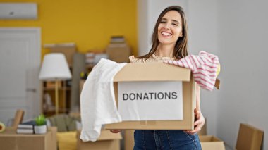 Genç, güzel, İspanyol bir kadın gülümsüyor. Kendine güvenen, yeni evinde bağışlanacak kıyafetlerle dolu bir paket tutuyor.