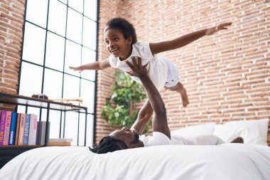 Father and daughter sitting on bed holding girl on air at bedroom