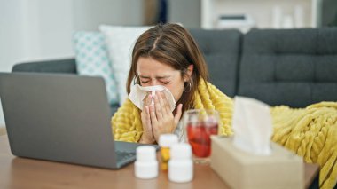 Genç ve güzel İspanyol kadın evde dizüstü bilgisayar ve mendil kullanarak yerde hasta yatıyor.