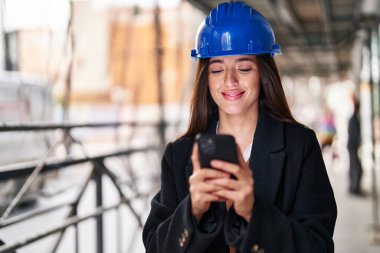 Young beautiful hispanic woman architect smiling confident using smartphone at street