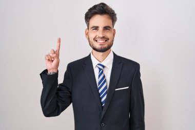 Dövmeli, takım elbiseli ve kravatlı genç İspanyol bir numarayı gösterip işaret ederken kendinden emin ve mutlu bir şekilde gülümsüyor.. 