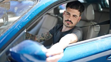 Latin kökenli genç adam dikiz aynasına dokunuyor. Sokakta arabada oturuyor.