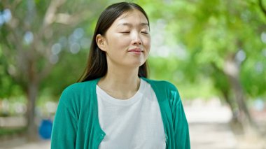 Parkta gözleri kapalı nefes alan genç Çinli kadın.