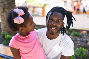 Father and daughter smiling confident sitting together on bench at park