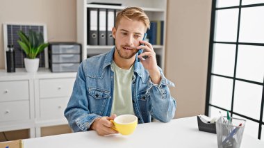 Kafkasyalı genç bir iş adamı akıllı telefonla konuşuyor ofiste kahve içiyor.