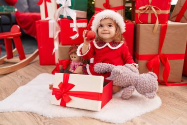 Sevimli sarışın bebek evde Noel ağacının yanında oturmuş hediyesini açıyor.