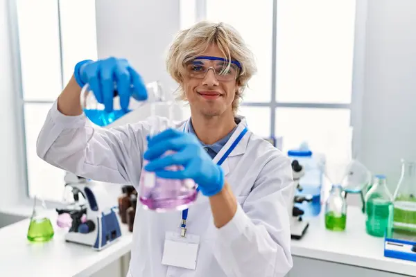 Young blond man scientist pouring liquid on test tube at laboratory