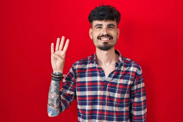 Mladý Hispánec Plnovousem Stojící Nad Červeným Pozadím Ukazující Ukazující Prsty — Stock fotografie