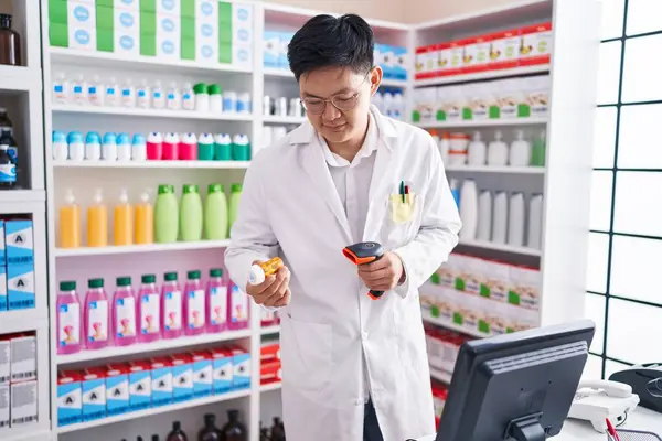 Young chinese man pharmacist smiling confident scanning pills bottle at pharmacy