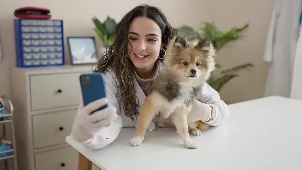 Young hispanic woman with dog veterinarian smiling confident having video call at clinic