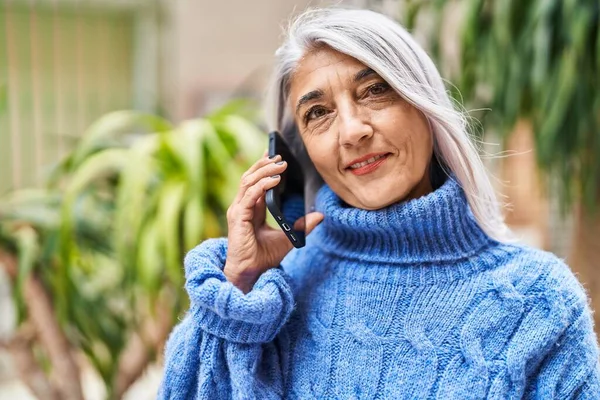 Middle age grey-haired woman smiling confident talking on smartphone at street