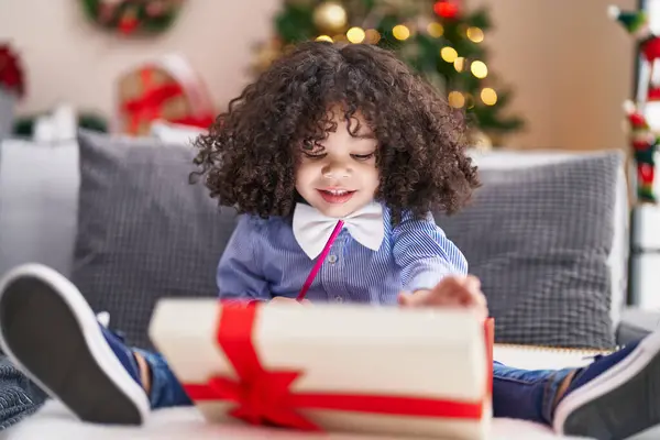 African american toddler unpacking gift sitting on sofa by christmas tree at home