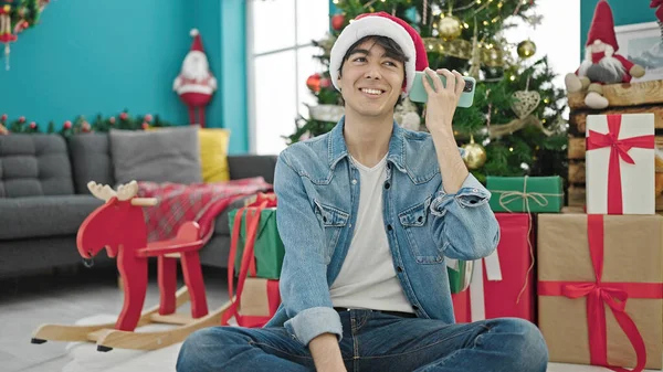 若いですヒスパニック男祝いクリスマスリスニング音声メッセージによってスマートフォンでホーム — ストック写真