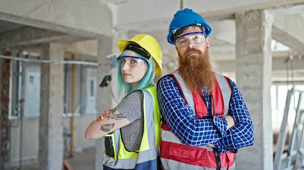 Man and woman builders standing with arms crossed gesture and relaxed expression at construction site