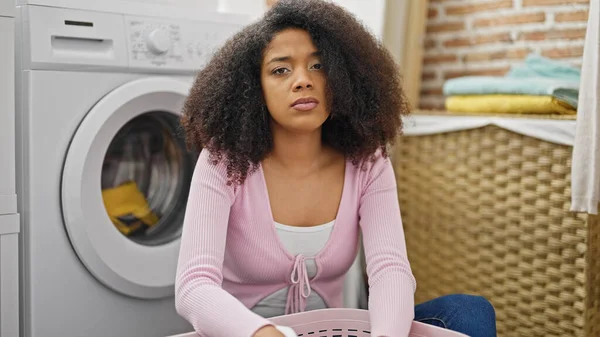 African american woman washing clothes looking upset at laundry room