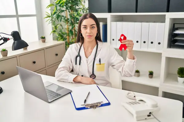 Hispanic Doctor Woman Holding Support Red Ribbon Thinking Attitude Sober — Stock Photo, Image