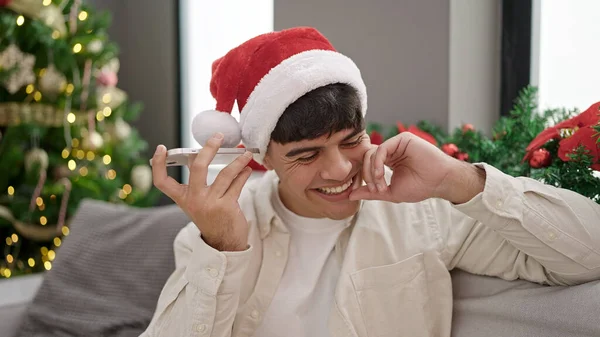 自宅でクリスマスを祝うスマートフォンで音声メッセージを聞く若いヒスパニックの男 — ストック写真