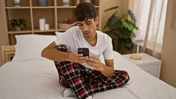 穿着睡衣 躺在舒适的床上休息的年轻人 沉浸在家里舒适的氛围中 在智能手机上输入着一个严肃的信息 — 图库照片