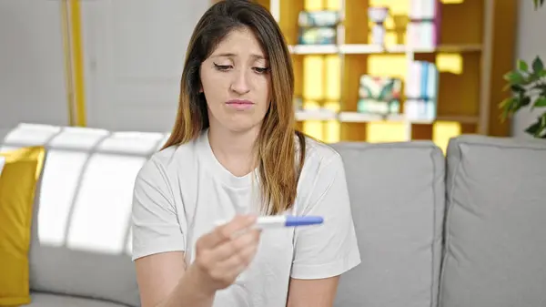 Young blonde woman holding pregnancy test looking upset at home