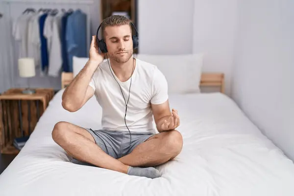 Young caucasian man doing yoga exercise sitting on bed at bedroom