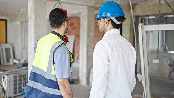 Two men builder and architect standing together backwards at construction site