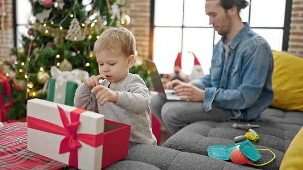 Father and son unpacking christmas gift using laptop at home
