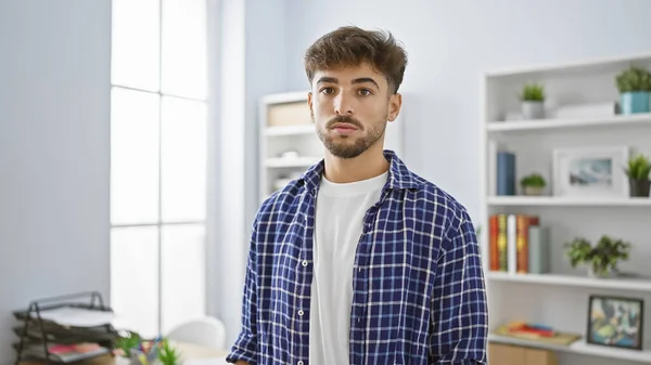 Elegant, serious young arab man standing confidently in the office, focused on his work. successful professional worker, showcasing his arabian and hispanic charm indoors.