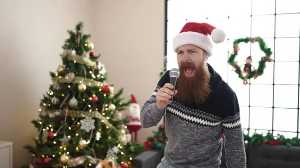Young redhead man singing song and dancing by christmas tree at home