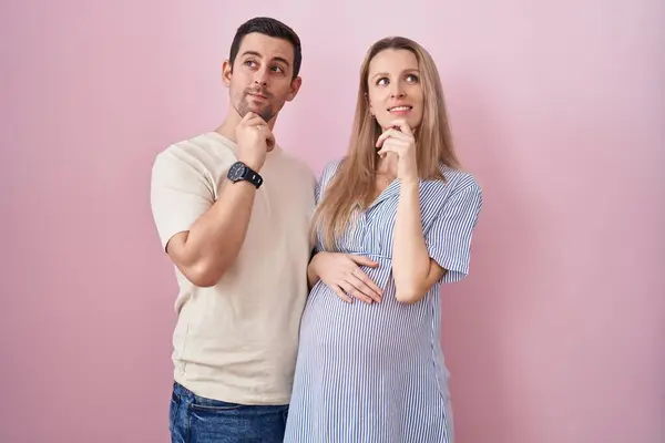 Casal Jovem Esperando Bebê Sobre Fundo Rosa Com Mão Queixo — Fotografia de Stock