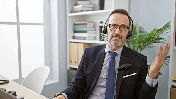 Middle age man with grey hair business worker wearing headset speaking at the office