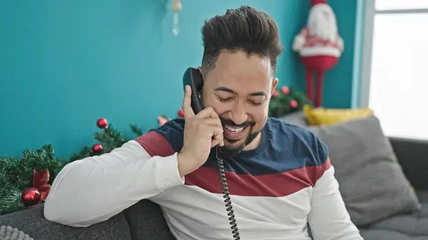Young latin man talking on telephone celebrating christmas at home