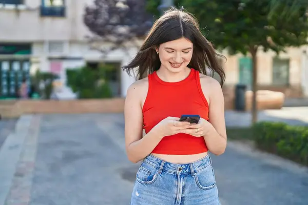 年轻的高加索女人在公园用智能手机充满自信地微笑 — 图库照片