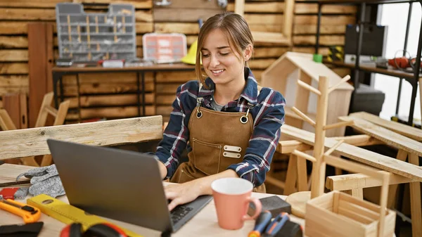 Smiling Young Blonde Woman Apron Skillfully Handling Laptop Woodwork Studio — Stock Photo, Image