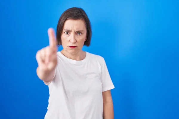 中世のヒスパニック女性立っている青の背景を指差す指アップと怒りの表現 ジェスチャーを示しません — ストック写真