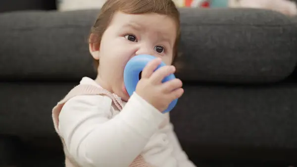 Adorable toddler bitting plastic hoop sitting on floor at home