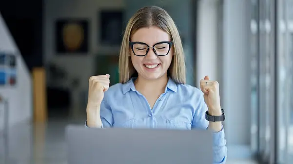 Young blonde woman business worker using laptop with winner gesture at office