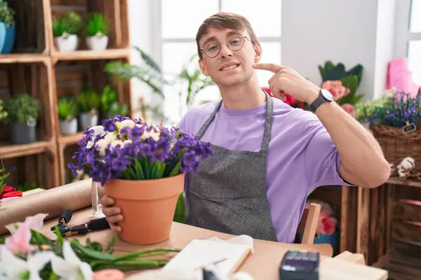花屋で働く白人ブロンドの男性は陽気な表情で微笑み 指の歯と口を指しています 歯科健康コンセプト — ストック写真